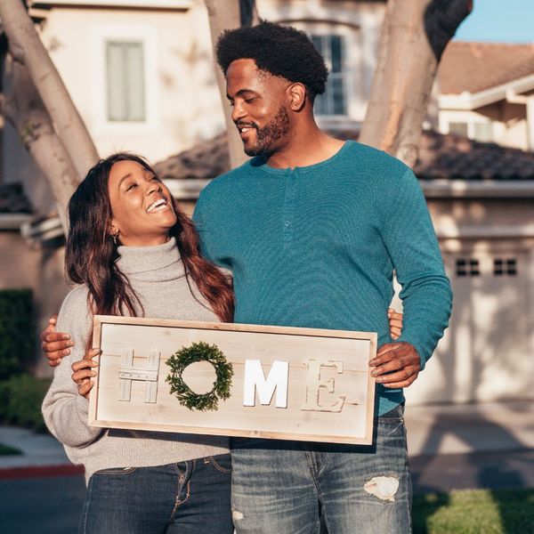 couple standing outside of home with home sign