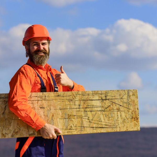 Roofing contractor smiles and gives thumbs up while holding plywood