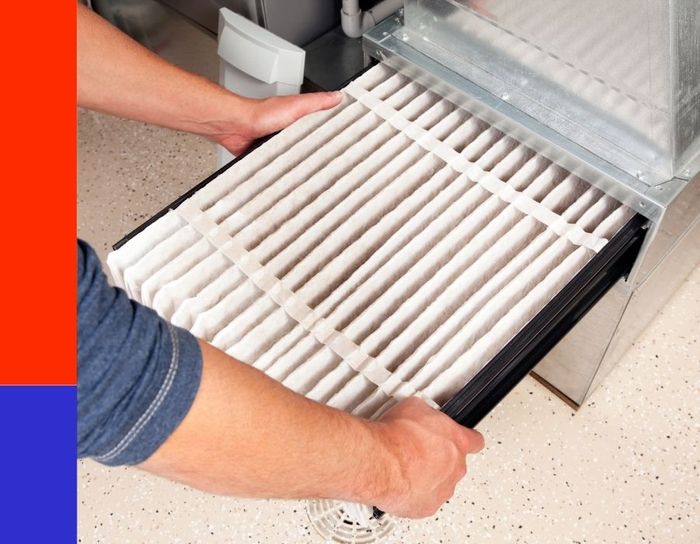 A technician's hands sliding a large, clean white pleated air filter into the filter rack of a residential heating system to ensure proper airflow and indoor air quality.