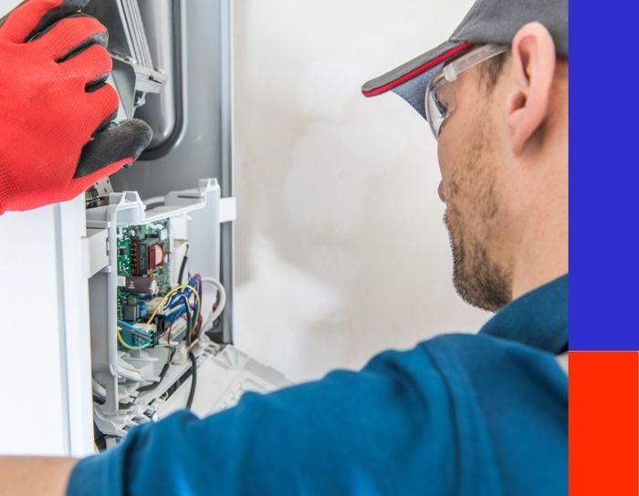 An HVAC specialist wearing safety glasses and a work cap meticulously inspecting the complex circuitry and wiring of a home heating system during a routine service call.