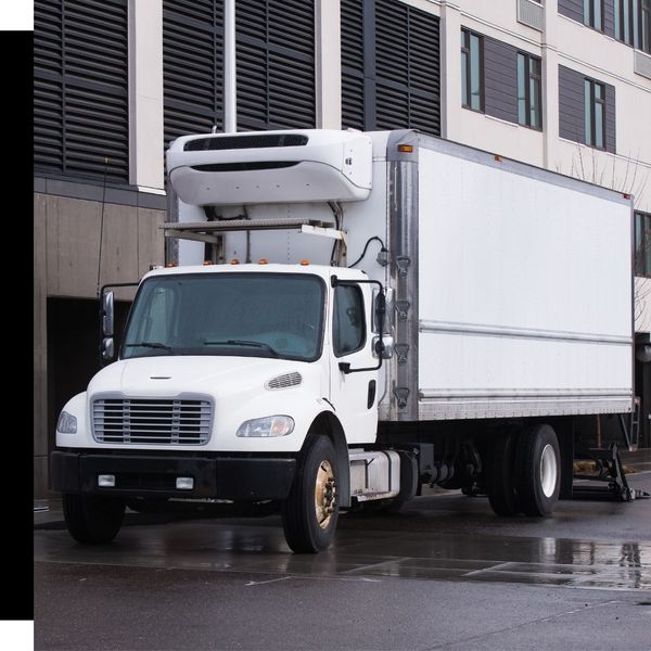 White refrigerated box truck parked next to a building