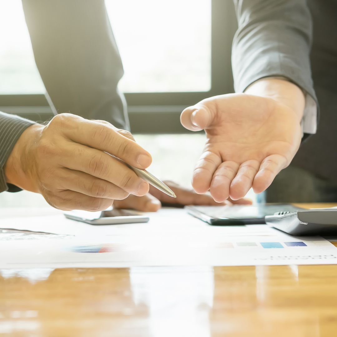 two business people gesturing at paper graphs on desk