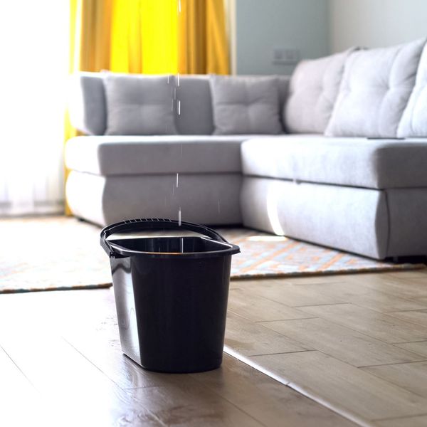 a bucket on the floor of a living room collecting dripping water