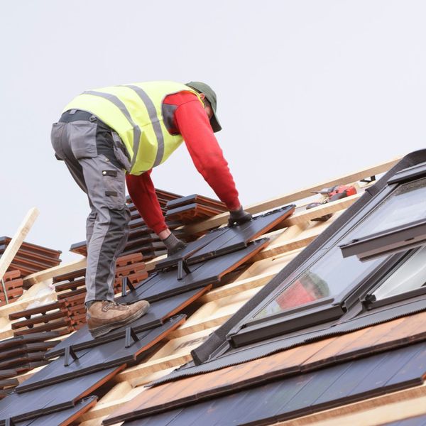 a roofer in safety gear, adding new roof tiles to a roof