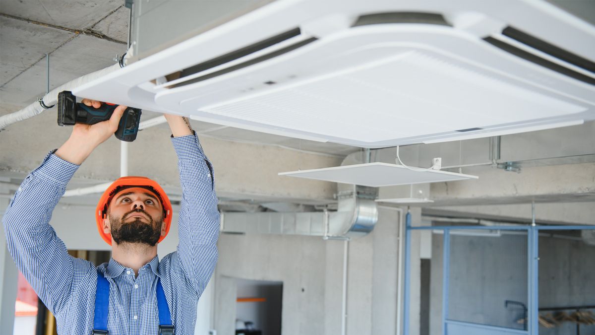 Technician performing air conditioner installation on ceiling AC unit in modern building