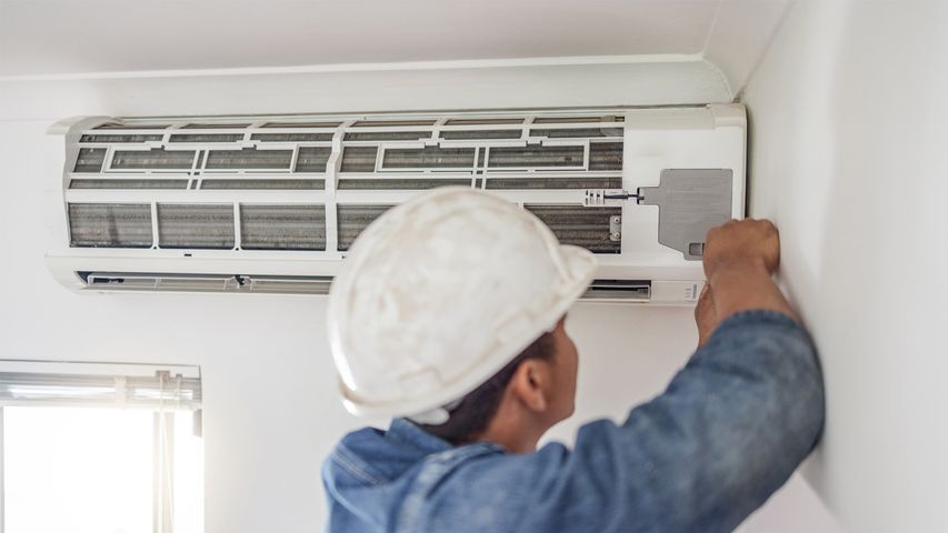 HVAC technician performing central AC maintenance on an indoor air conditioning unit