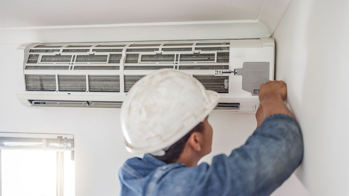 HVAC technician performing central AC maintenance on an indoor air conditioning unit