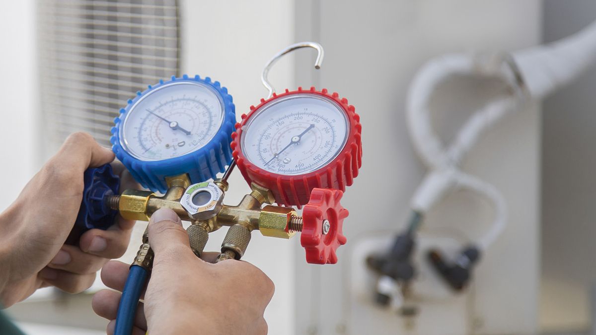 HVAC technician checking AC system pressures with manifold gauges next to an outdoor unit during an AC repair visit in Greenacres, FL