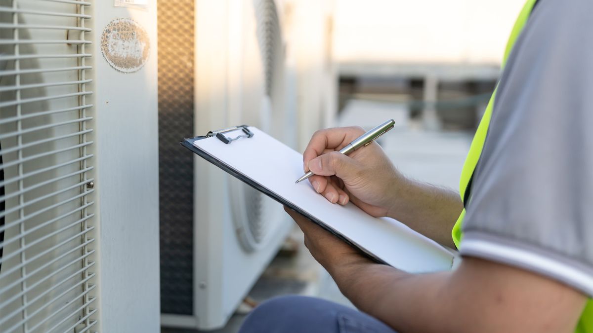 HVAC technician with a clipboard inspecting a row of outdoor AC condenser units