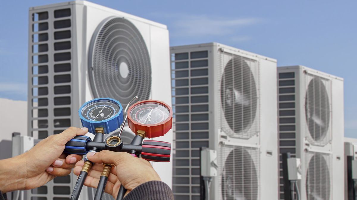Technician checking system pressures with manifold gauges in front of commercial VRF/VRV outdoor units on a rooftop