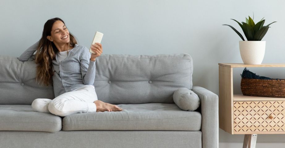 woman on couch with AC remote, smiling