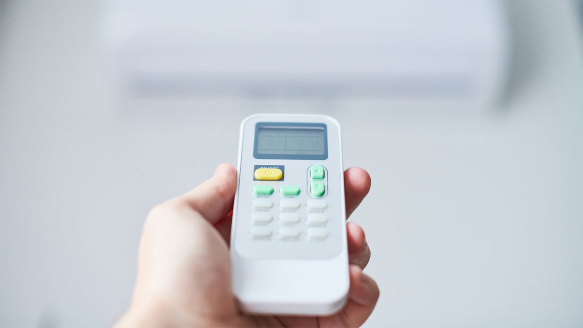 Hand holding an AC remote control pointed at a wall-mounted indoor unit in a home in Davie, FL