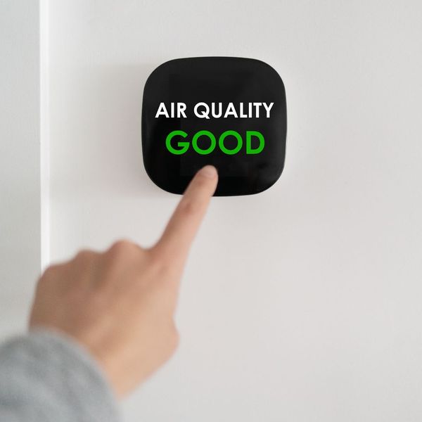 Person pointing to an air quality monitor that says "Air Quality Good."