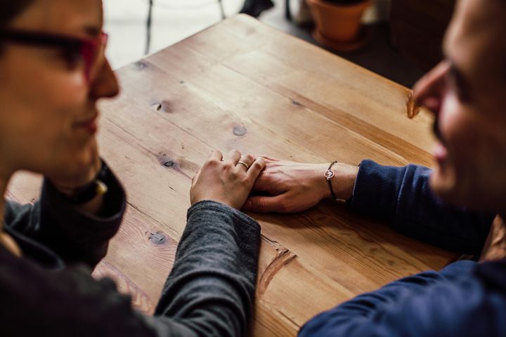 Partners holding hands across a wooden table, illustrating connection amid therapeutic conversation.