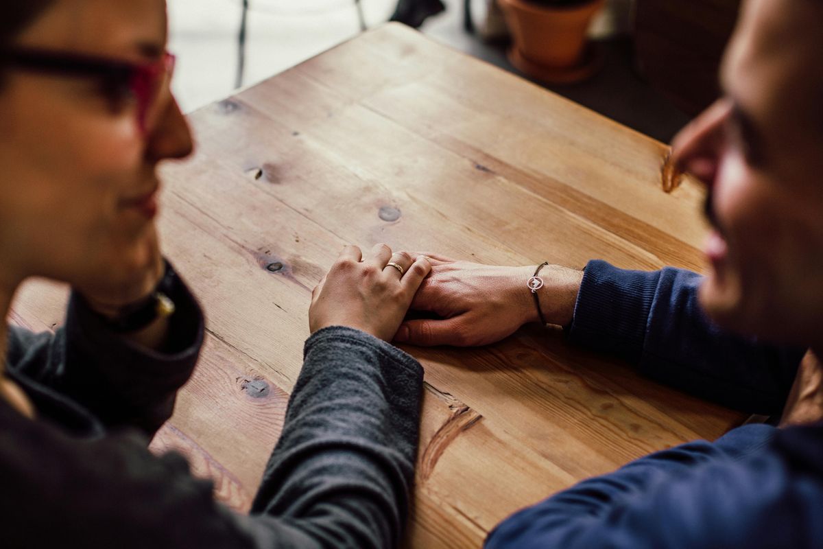Partners holding hands across a wooden table, illustrating connection amid therapeutic conversation.