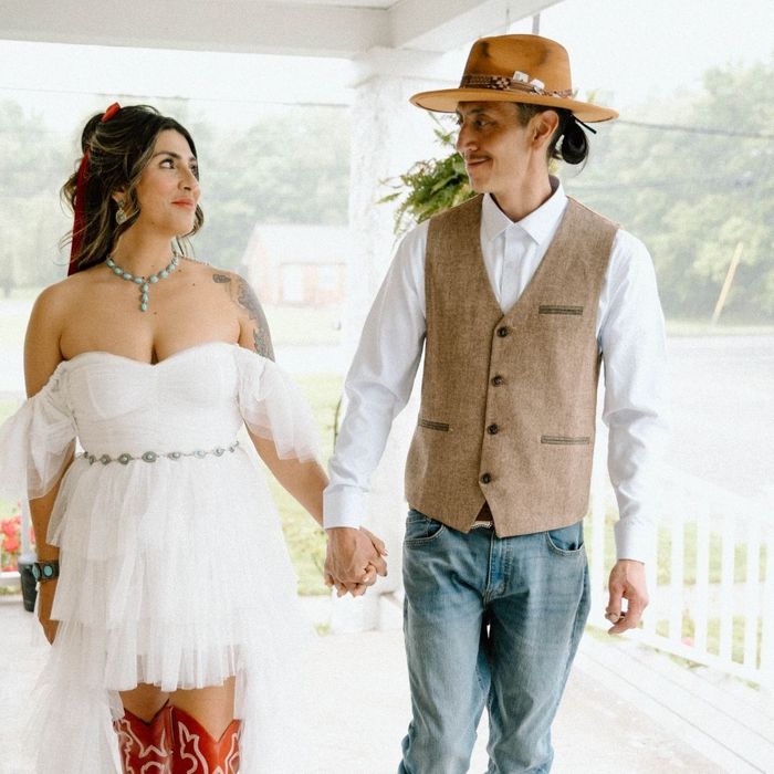 Bride wearing boots and groom in a cowboy hat holding hands while walking