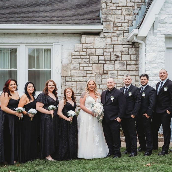 Bride and groom posing outdoors with their groomsmen and bridesmaids dressed in black