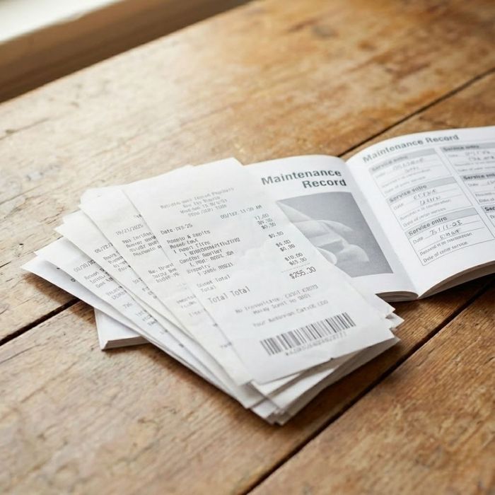 A stack of maintenance receipts and a service booklet on a workshop counter.