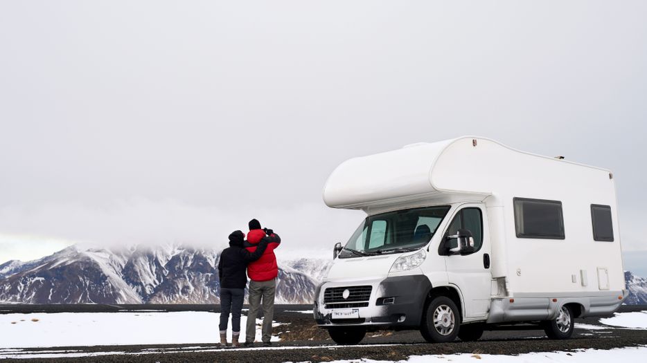 Couple taking picture of snowy mountain outside their RV