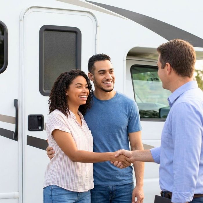 A couple smiles while shaking hands near a closed RV door.