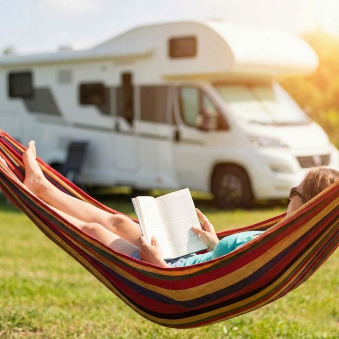 A person relaxes in a hammock with a book, enjoying free time with a motorhome in the background.