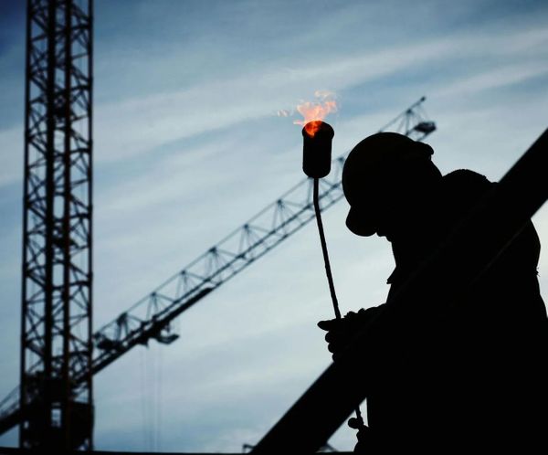 Silhouette of a construction worker using a torch with a crane in the background