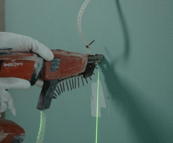 Hand using an automatic screw gun to install drywall with laser guidance