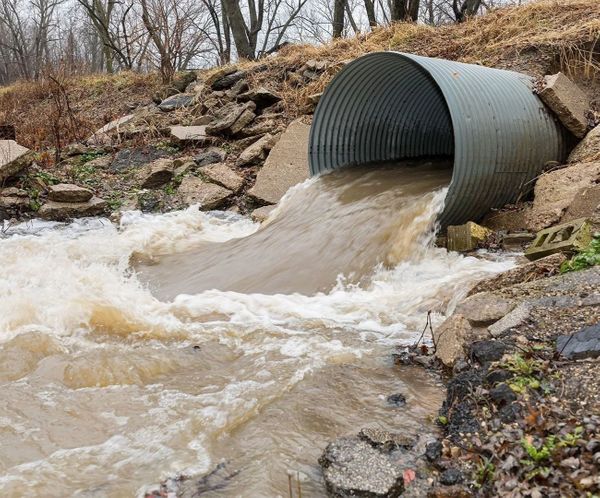 Large corrugated pipe discharging muddy stormwater runoff into a stream