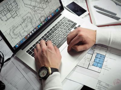 Hands typing on a laptop with architectural blueprints for construction design