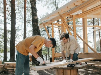 Two construction workers cutting wood for a new home frame in a wooded area