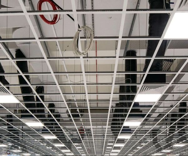  Underside view of a commercial suspended ceiling grid with exposed wires and ducts