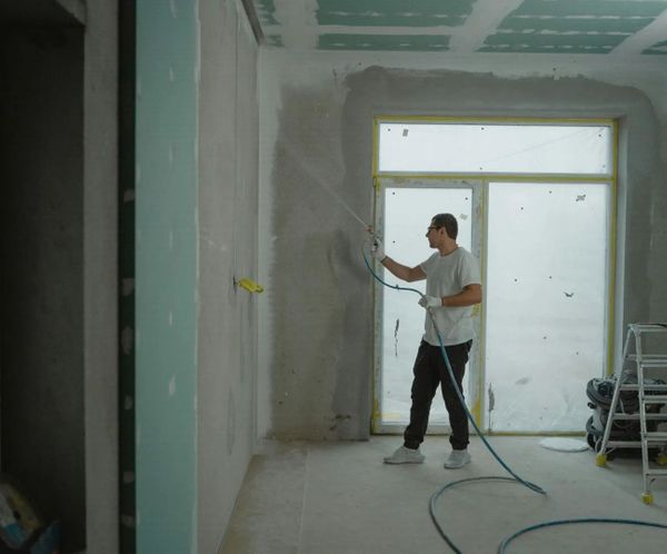 Construction worker spray painting new drywall in a commercial building