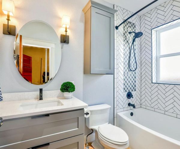 Remodeled bathroom with gray vanity, round mirror, and subway tile shower Remodeled bathroom with gray vanity, round mirror, and subway tile shower
