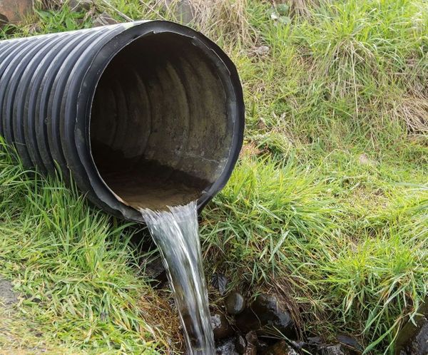 Black corrugated pipe with clean water draining onto green grass