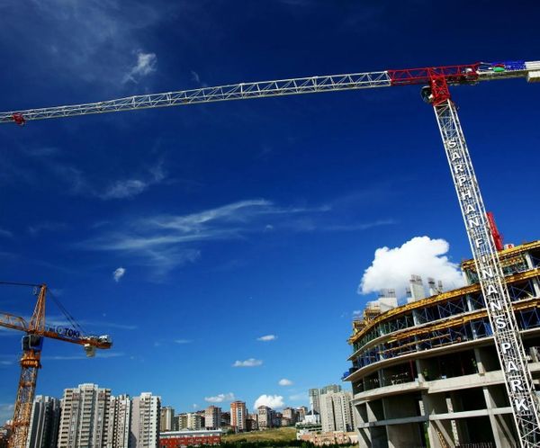 Large tower cranes at a commercial high-rise construction site against blue sky