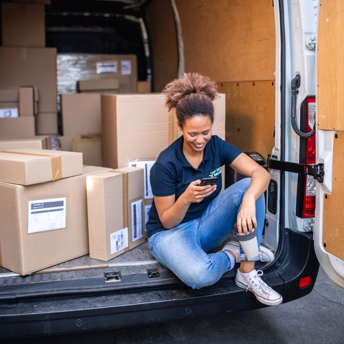 Delivery woman sitting in back of truck and smiling