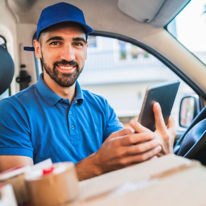 Delivery driver sitting in their van smiling holding a tablet