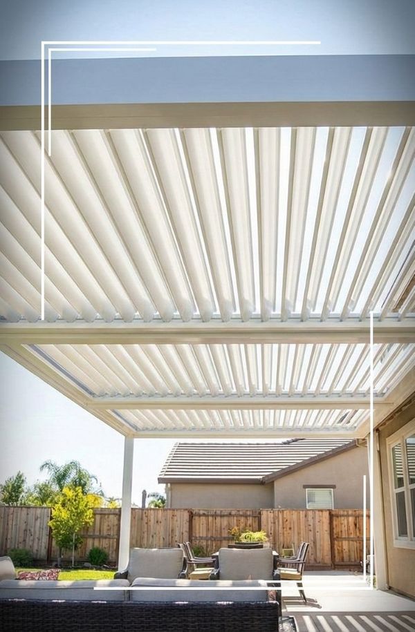 Modern white louvered pergola in a sunny backyard with patio furniture, showing louvers partially open.