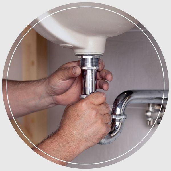 Close-up of a plumber's hands installing and tightening a chrome P-trap pipe assembly under a white bathroom sink.