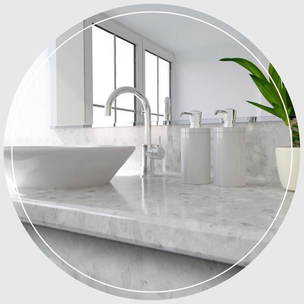 A modern bathroom vanity featuring a white vessel sink, polished chrome faucet, marble countertop, and soap dispensers.