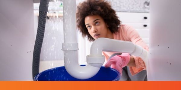 woman looking at leaking pipes underneath sink