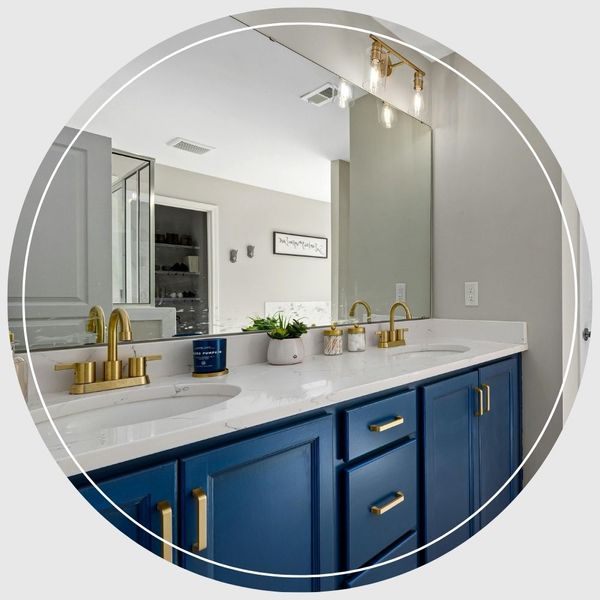 A newly remodeled bathroom vanity featuring deep blue cabinets, a marble countertop, brass faucets, and a large mirror.