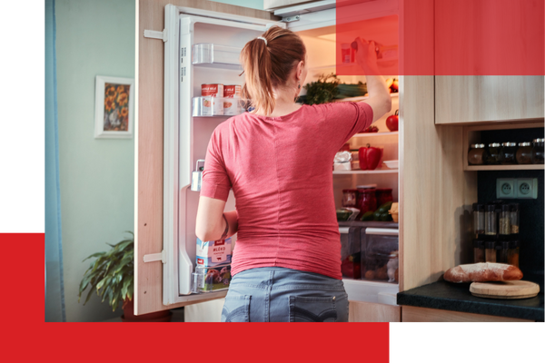 A woman from behind is reaching into a well-stocked refrigerator, which is filled with various groceries and fresh produce, in a brightly lit kitchen. A woman from behind is reaching into a well-stocked refrigerator, which is filled with various groceries and fresh produce, in a brightly lit kitchen.