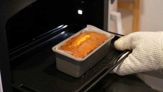 A hand with an oven mit putting a load of bread into an oven A hand with an oven mit putting a load of bread into an oven