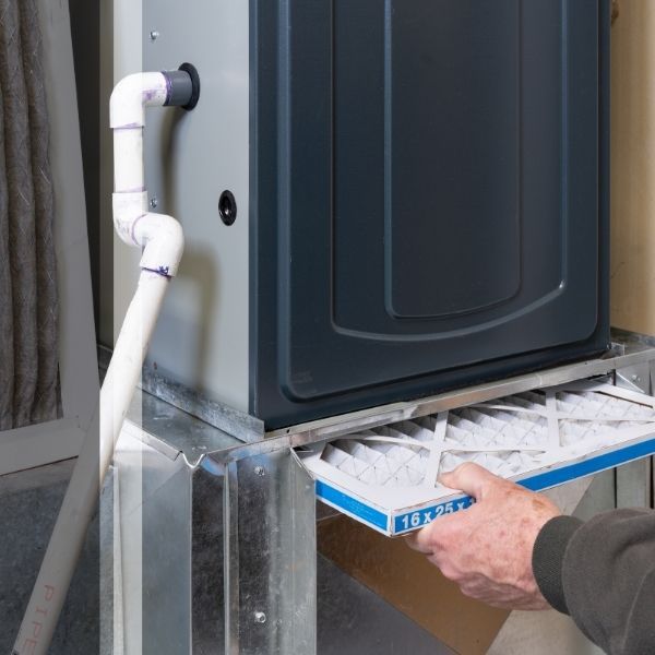 Close-up of a technician's hand replacing a clean 16x25x1 air filter in a residential furnace system to improve home air quality and heating efficiency.