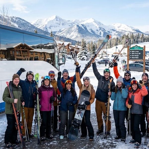 group of colleagues or friends standing together holding skis and snowboards, smiling and cheering