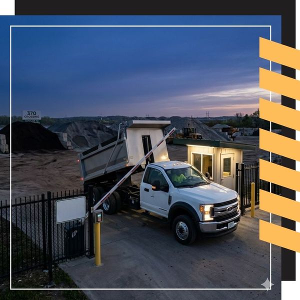 A dawn photograph showing the secure entrance of a facility, as the automated gate begins to lift for a commercial dump truck