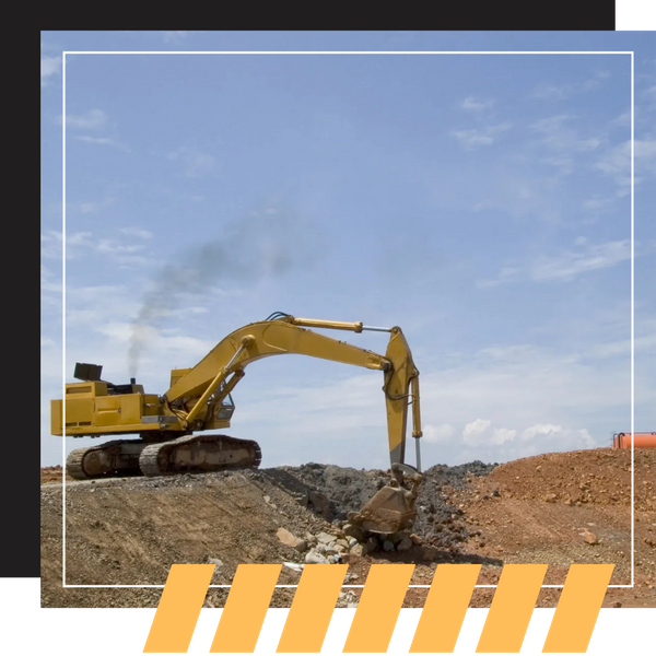 A yellow excavator working on a dirt mound, emitting dark exhaust smoke against a blue sky.