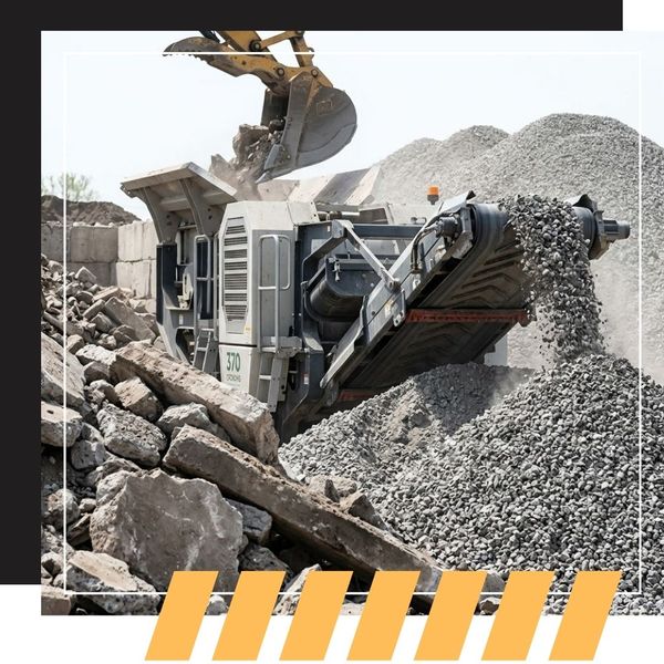 A powerful industrial crushing machine actively processes large concrete debris into a new, coarse recycled concrete aggregate stockpile
