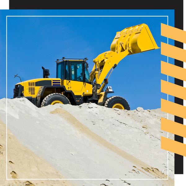 A yellow front-end loader parked on the crest of a large sand or fine gravel pile.